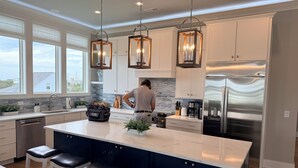 A modern kitchen with a large island, stainless steel appliances, pendant lighting, and a view of the outdoors. - Soundfront hot tub and rooftop deck (Surf City)