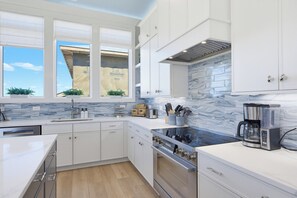 A modern kitchen with white cabinetry, a marble backsplash, and a large window with blinds. - Soundfront hot tub and rooftop deck (Surf City)