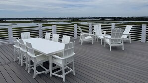 A deck with white chairs and a table, overlooking a water body and distant landscape. - Soundfront hot tub and rooftop deck (Surf City)