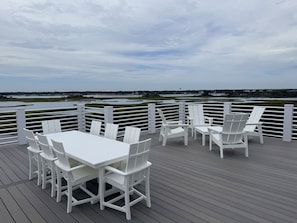 Eine Terrasse mit weißen Stühlen und einem Tisch, mit Blick auf ein Gewässer und eine entfernte Landschaft.
