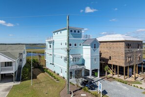 A multi-story building with a prominent central tower, a covered porch, and a view of a body of water. - Soundfront hot tub and rooftop deck (Surf City)