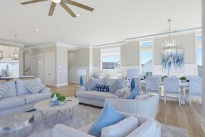 A spacious living room with a high ceiling, a dining area with white furniture, and a kitchen with modern appliances. - Soundfront hot tub and rooftop deck (Surf City)