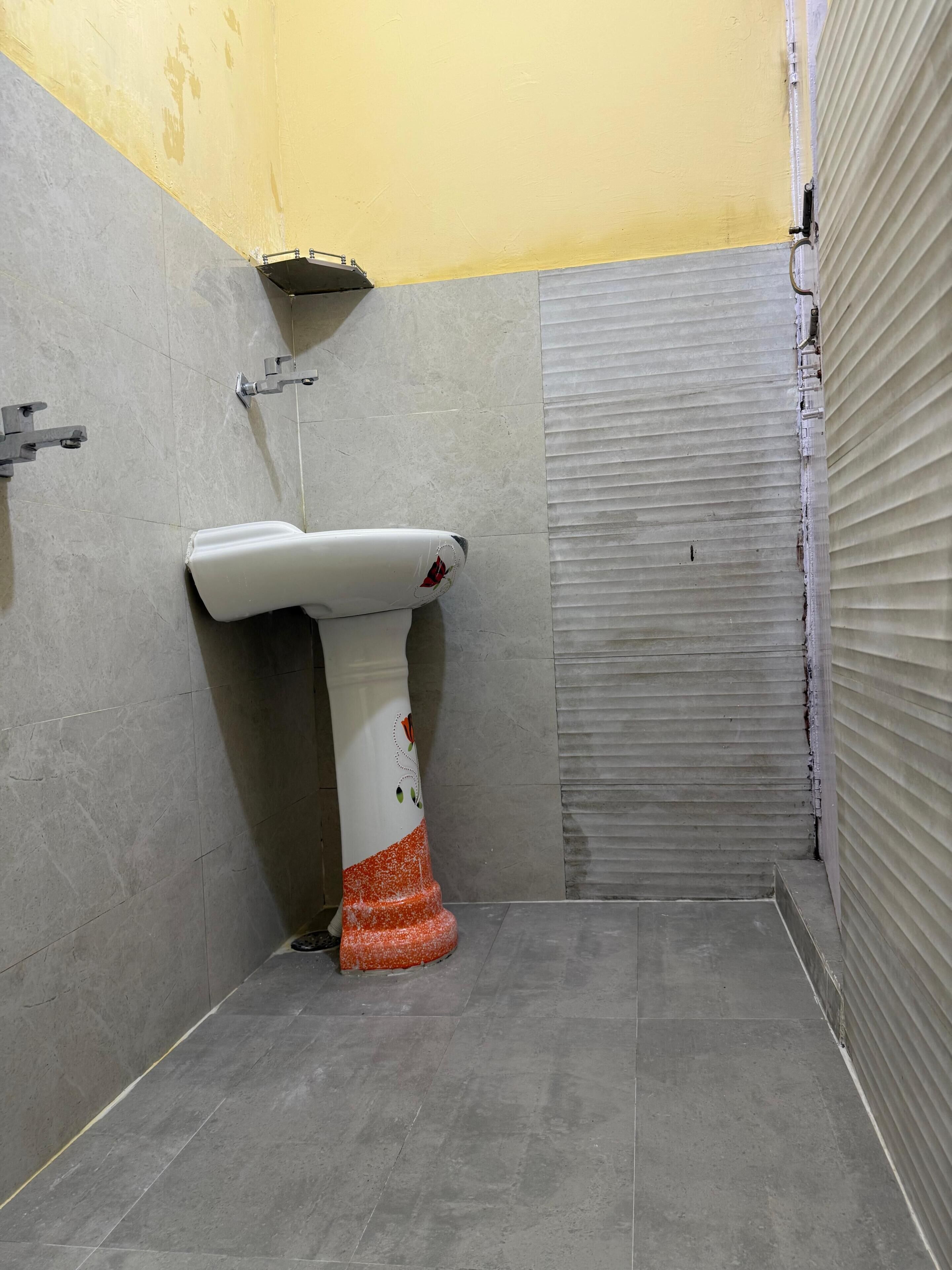 A bathroom with a white pedestal sink, a yellow wall, and a closed shutter door.