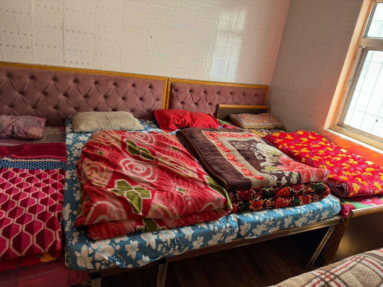 A bedroom with a tufted headboard, multiple beds, and a variety of blankets and pillows.