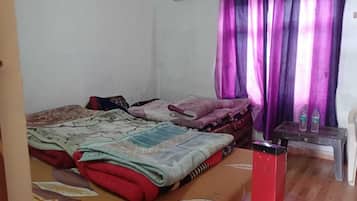 Un dormitorio con dos camas, suelo de madera, una cortina y una mesita con botellas.