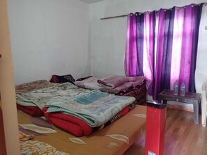 A bedroom with two beds, a wooden floor, a curtain, and a small table with bottles.
