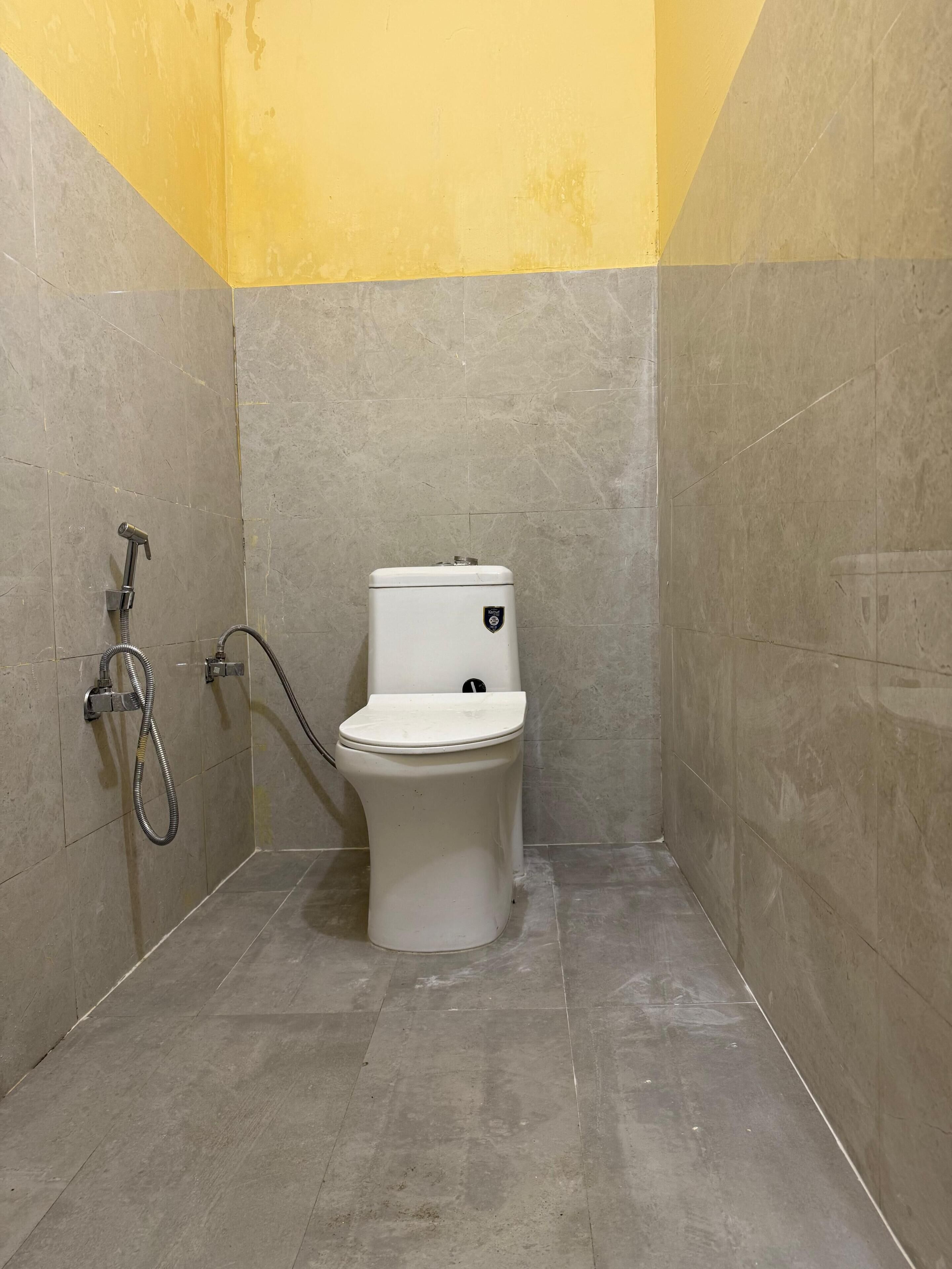 Une petite salle de bain fermée, équipée de toilettes, d’une douche et d’un tuyau d’eau.