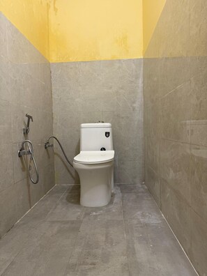 A small, enclosed bathroom with a toilet, a shower, and a hose.