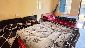 A room with a bed, a window with curtains, a wall-mounted light switch, and a small mirror.