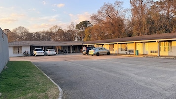 A motel with a covered parking area, a single-story building, and a grassy area.