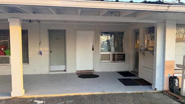 A covered porch with a door marked '100', a window with a view, and a small air conditioning unit.