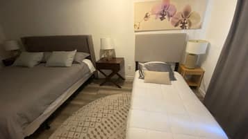 Ein Hotelzimmer mit zwei Betten, einem Nachttisch mit Lampen, einem gemusterten Teppich und einem floralen Gemälde an der Wand.