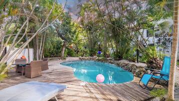 Eine Holzterrasse umgibt einen Swimmingpool mit Liegestühlen und einem Tisch.