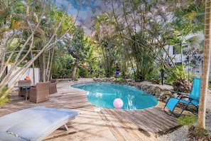Una terraza de madera rodea una piscina con sillones de descanso y una mesa.