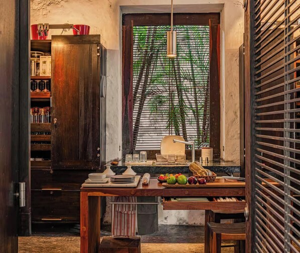 A kitchen with a wooden cabinet, a dining table with fruit, and a window with blinds.