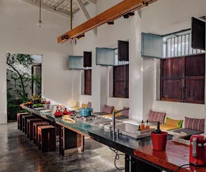 A modern kitchen with a long island, bar stools, and a dining area with a view of greenery.