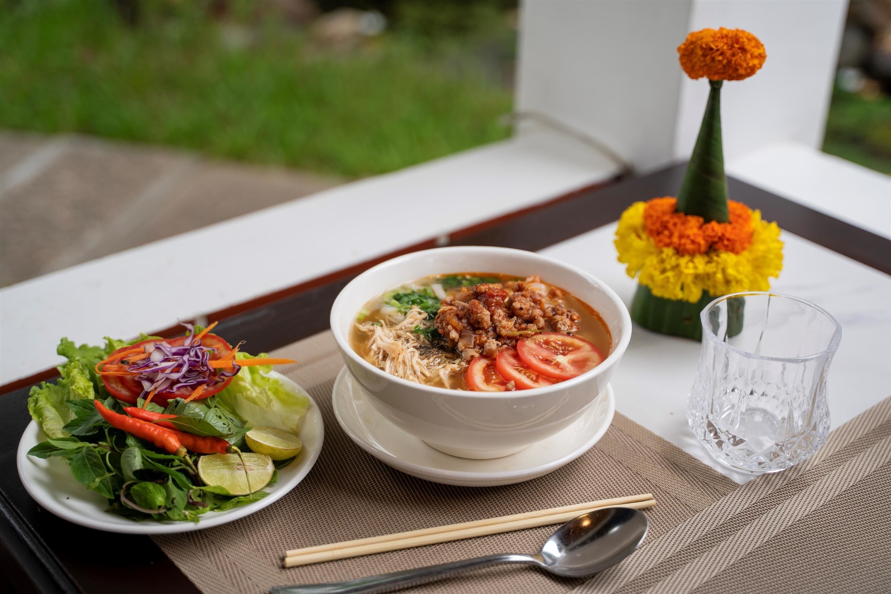 A table with a bowl of soup, a salad, and a glass of water, with a flower arrangement in the background.