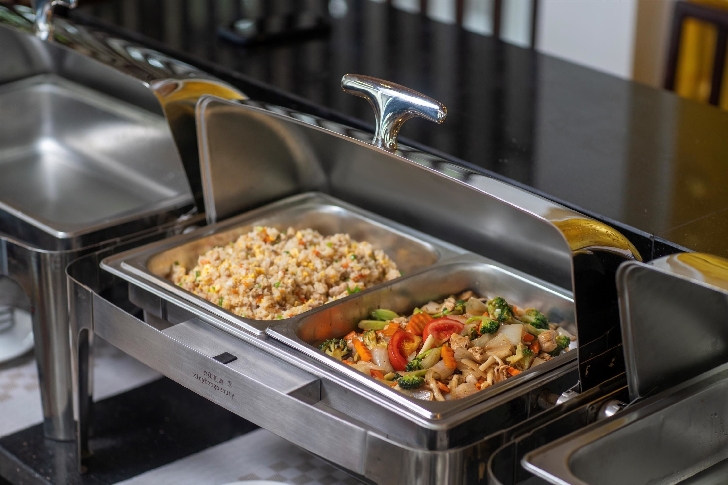 A buffet with two food dispensers, one with fried rice and the other with stir-fried vegetables.