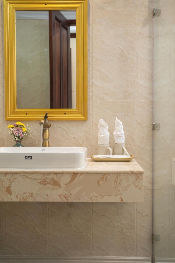 A bathroom with a marble sink, a gold-framed mirror, and a vase of flowers.
