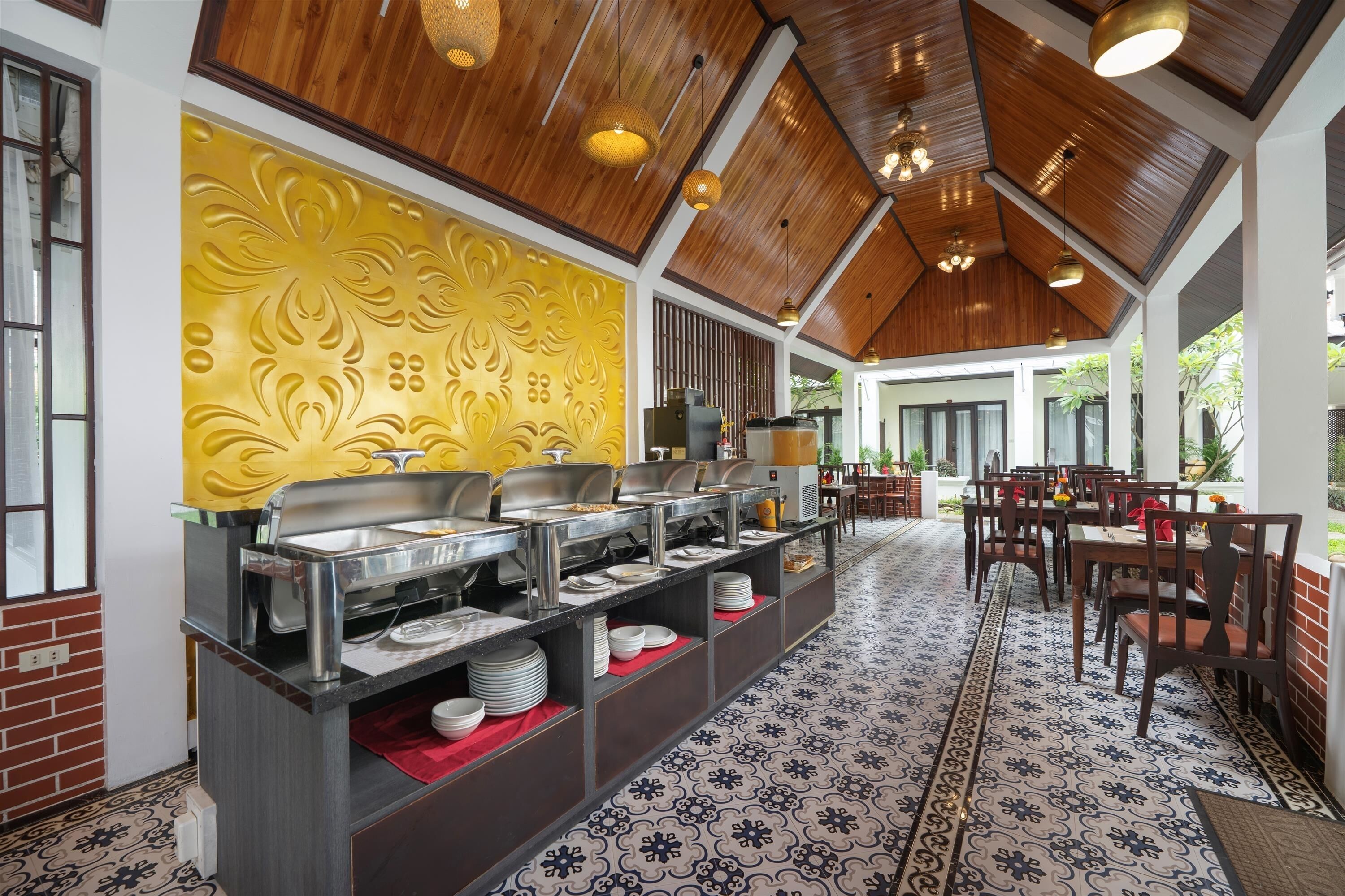 A buffet area with stainless steel serving counters, a decorative wall with a floral pattern, and a dining area with wooden chairs and tables.