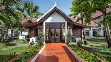 A traditional building with a tiled entrance, surrounded by lush greenery and palm trees.