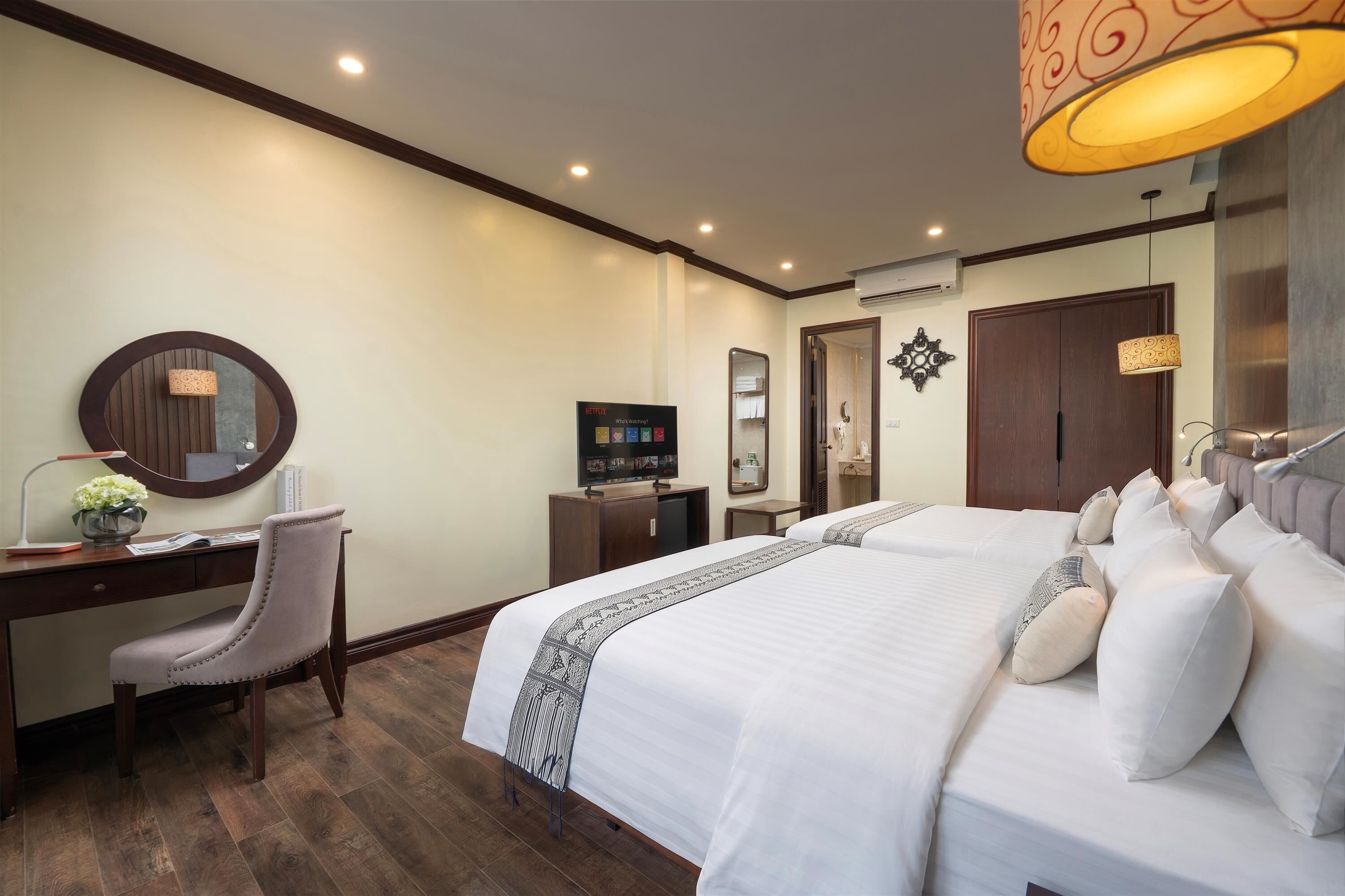 A hotel room with a large bed, a desk with a chair, a television, and a mirror.