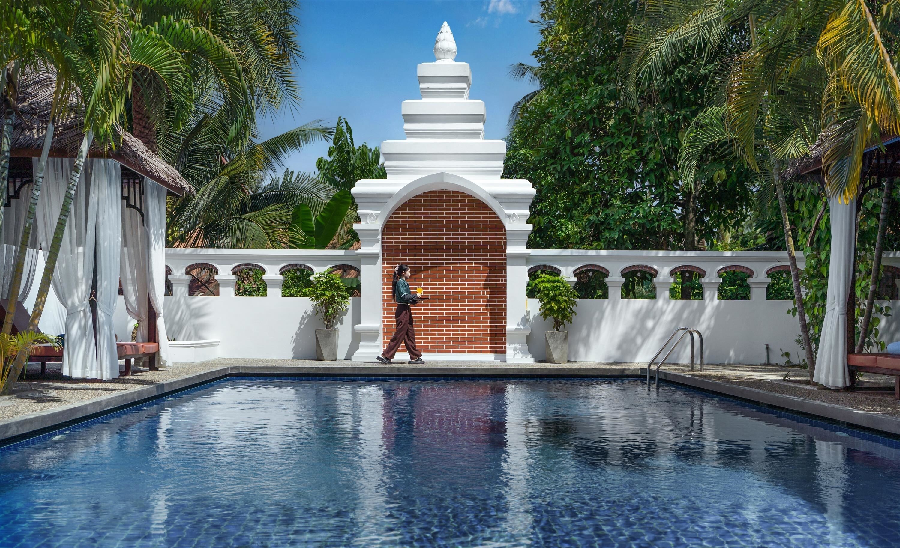 A swimming pool with a white structure in the background, surrounded by greenery.
