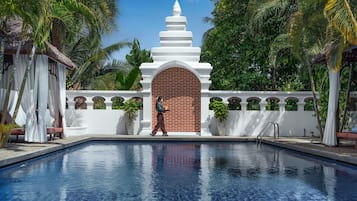 A swimming pool with a white structure in the background, surrounded by greenery.