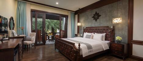 A bedroom with a large bed, a desk, and a chair. There is a sliding glass door leading to a balcony.