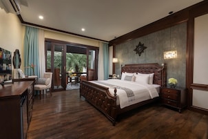 A bedroom with a large bed, a desk, and a chair. There is a sliding glass door leading to a balcony.