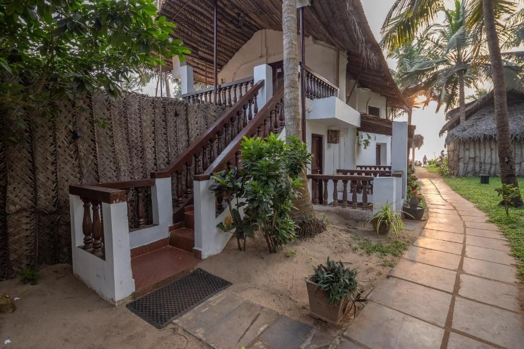 A traditional house with a wooden staircase, a thatched roof, and a paved walkway.