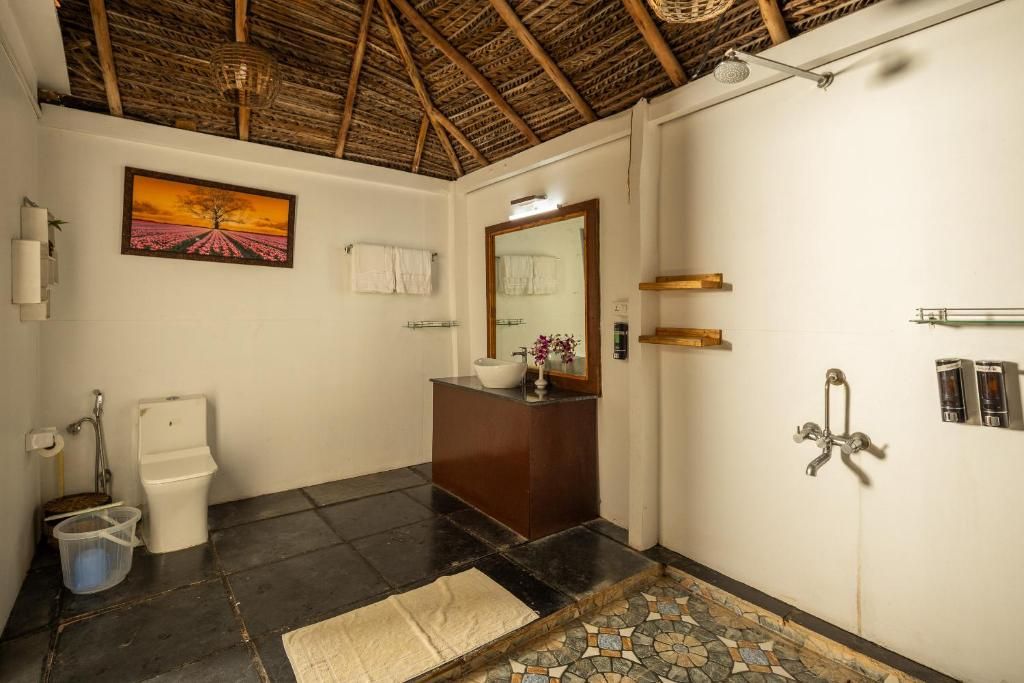 A bathroom with a tiled floor, a wooden ceiling, a white toilet, a wooden vanity, a mirror, and a shower with a metal faucet.