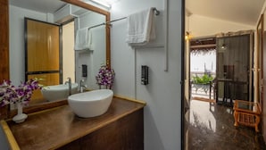 Ein Badezimmer mit einem großen Spiegel, einem weißen Waschbecken und einer Holzwirtschaft. An der Wand ist ein Handtuchhalter und in der Nähe des Eingangs ein kleiner Hocker.