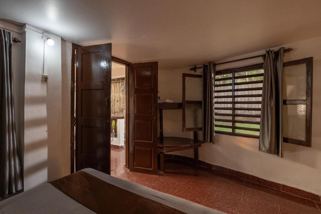 A room with a bed, a wooden door, a window with blinds, and a shelf unit.