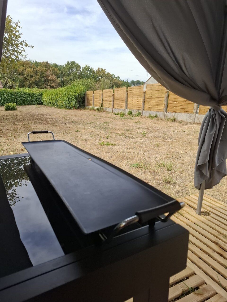 Blick auf einen überdachten Außenbereich mit Grill und einer Holzterrasse.