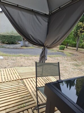 Uma área de pátio com mesa e cadeiras, um deck de madeira e um toldo cinzento.