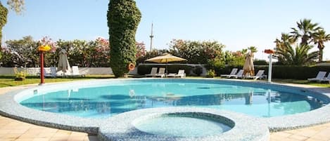 Una piscina con hidromasaje, rodeada de sillones de descanso y palmeras.