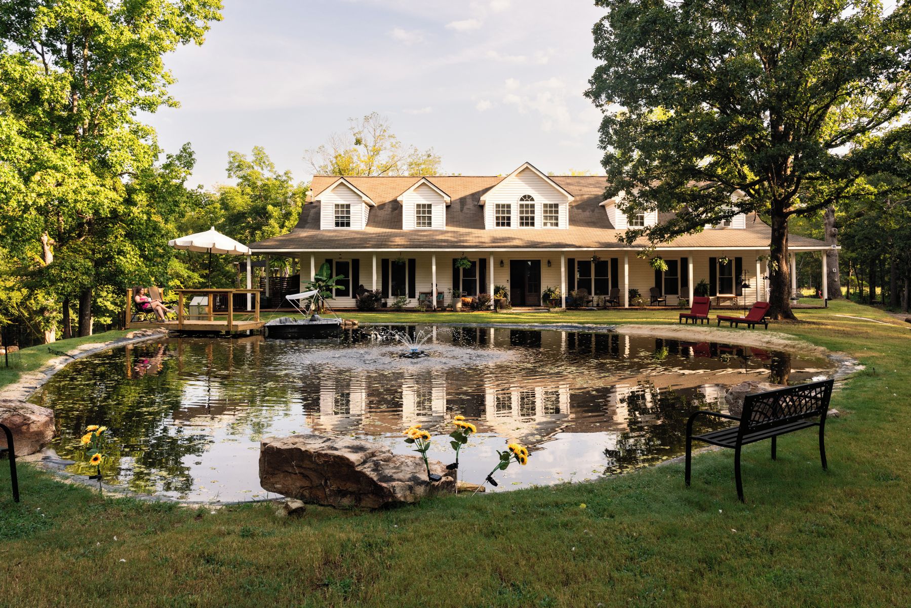 A large house with a pond, outdoor seating, and a lawn.