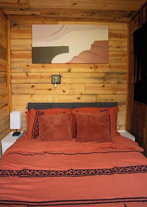 Une chambre rustique en bois, avec un lit, une table de chevet, une lampe et un tableau au mur.