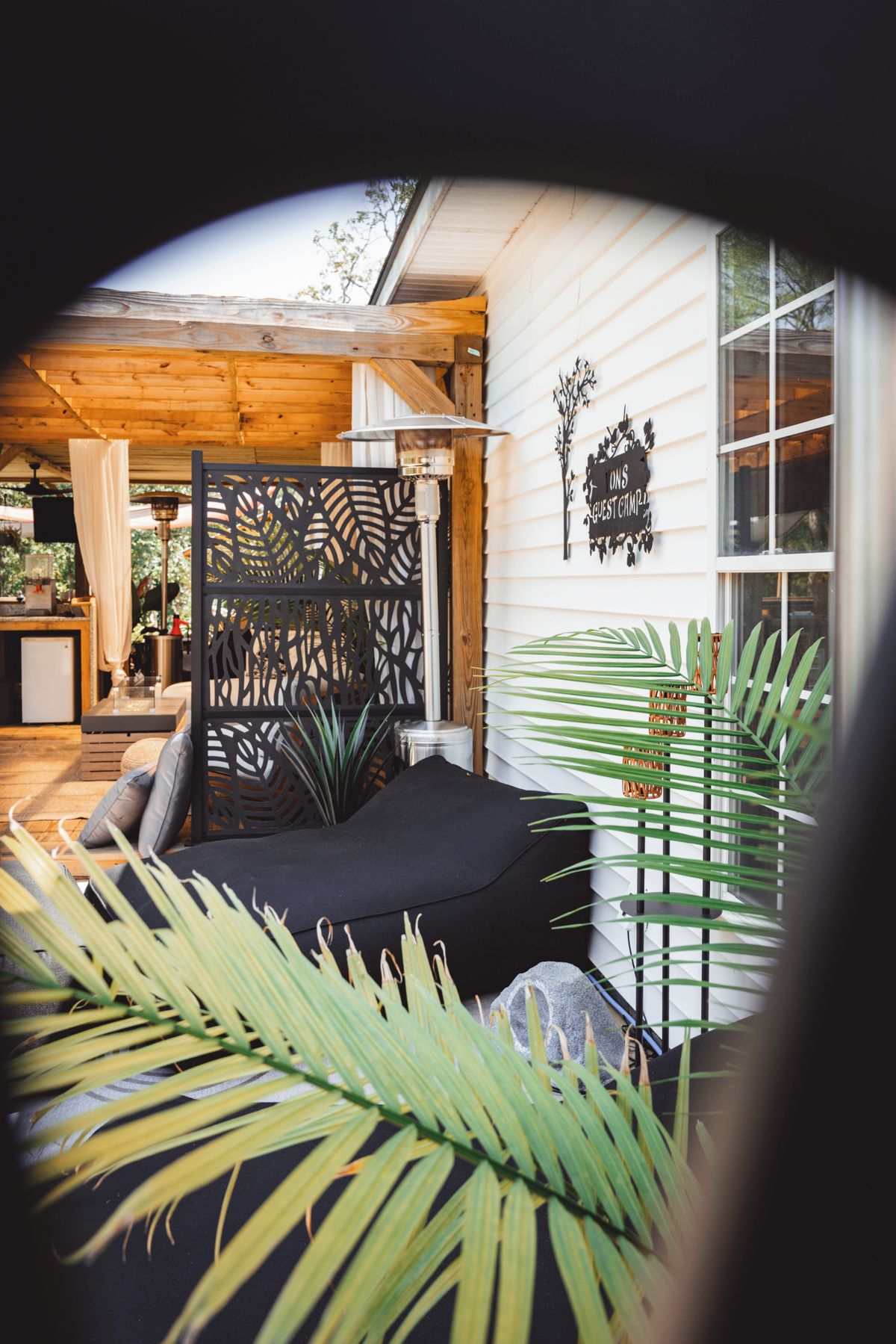 A cozy outdoor seating area with a black cushioned bench, a decorative metal fence, and lush green plants.