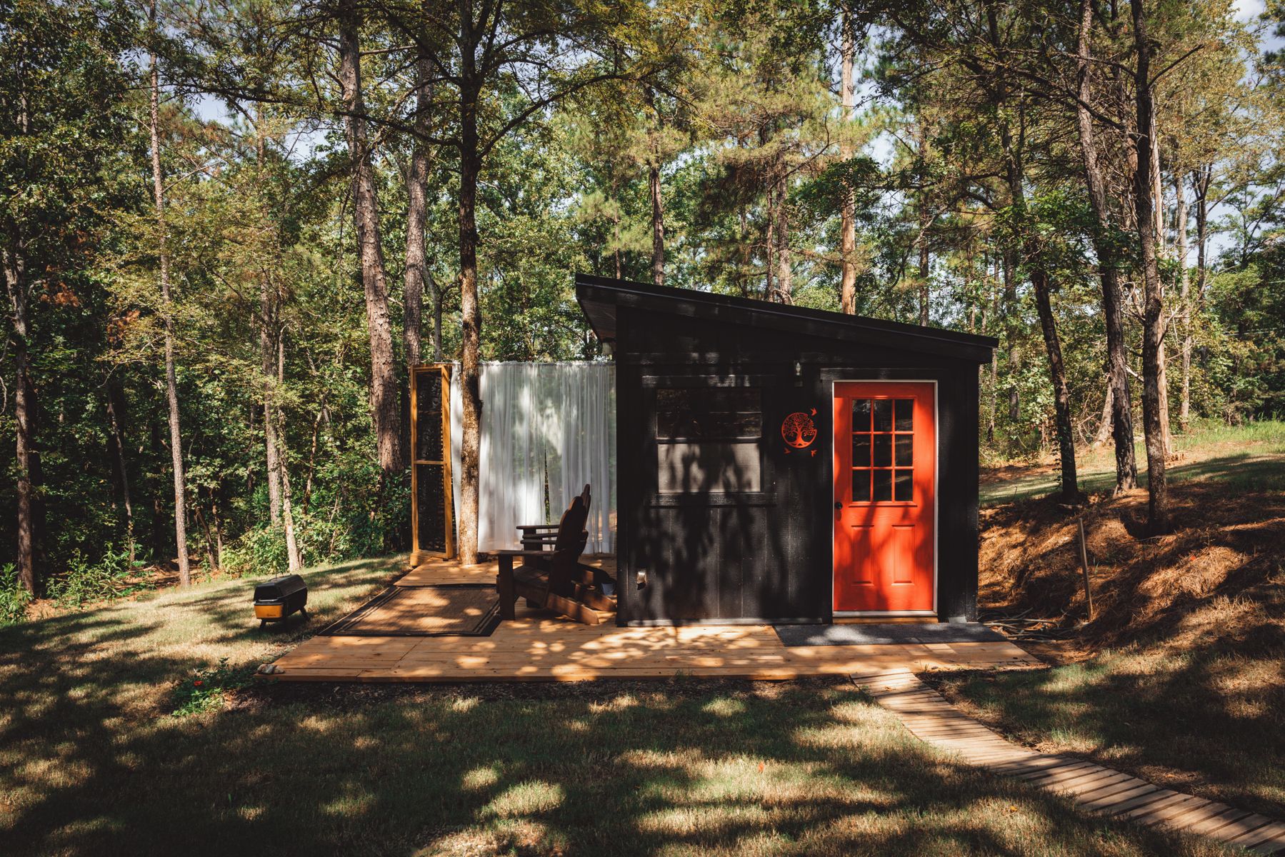 A small cabin with a red door, a bench, and a covered area with a white curtain.