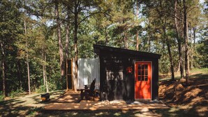A small cabin with a red door, a bench, and a covered area with a white curtain.