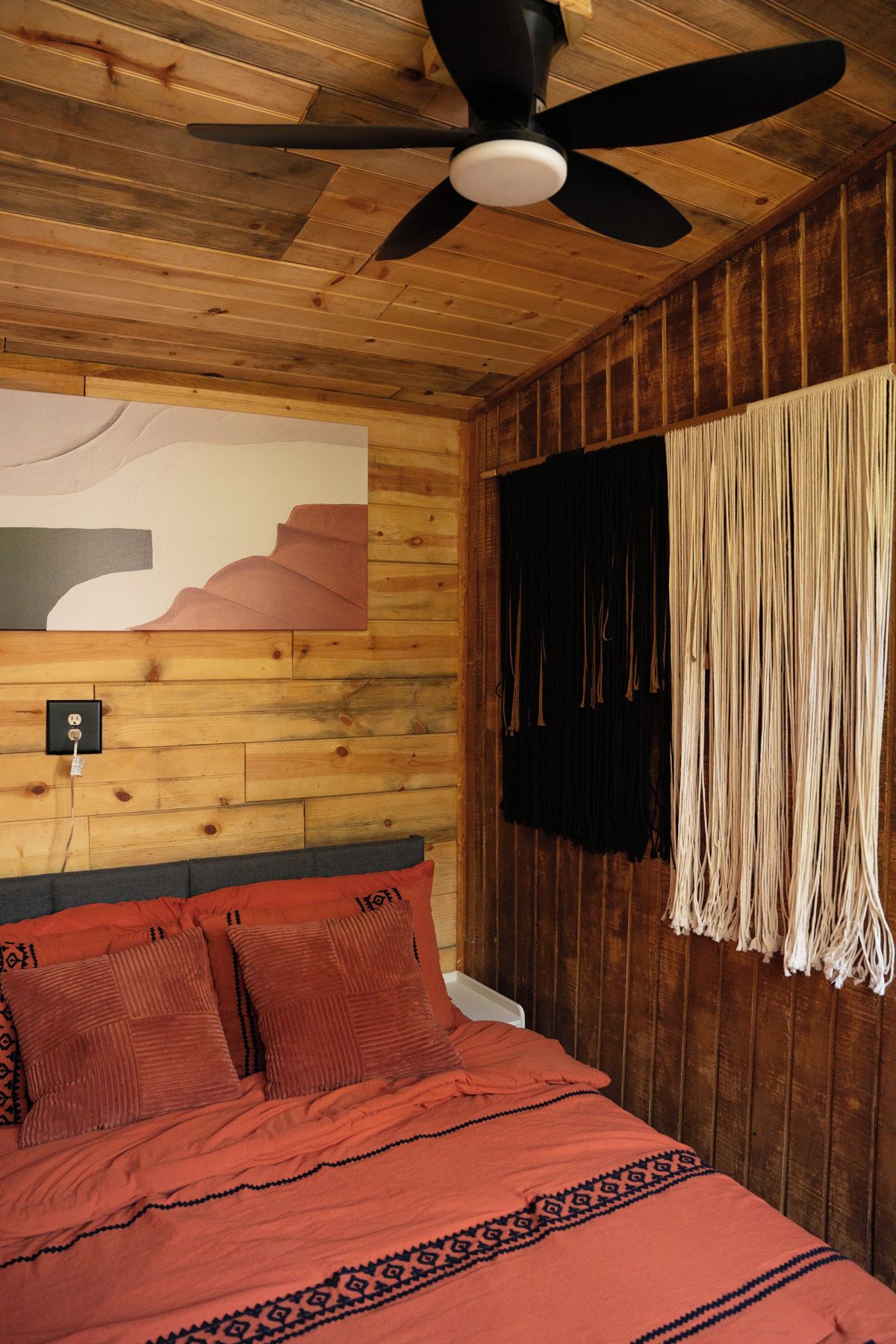 A room with a bed, a ceiling fan, a wall with a painting, and a curtain.