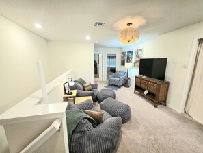 A living room with a white staircase, grey upholstered seating, a wooden entertainment unit, and a flat-screen TV. - Windsor Island 5BR Disney Home: Pool & Waterpark (Davenport)