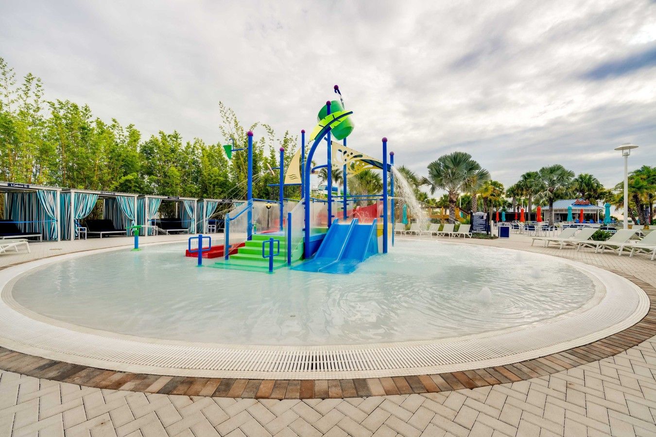 A water play area with slides and steps, surrounded by a pool and lounge chairs.