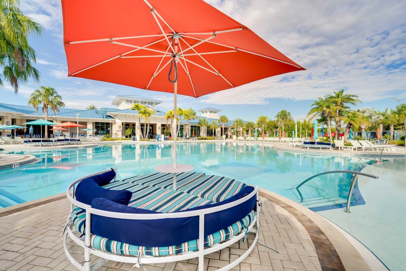 Un área de piscina con un espacio de estar circular, sillones reclinables y sombrillas.
