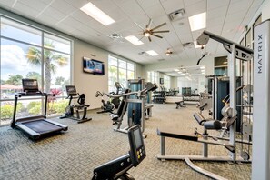 Ein Fitnessstudio mit Cardiogeräten, Gewichten und einem großen Fenster mit Blick auf Palmen.