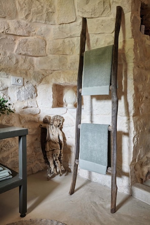 A rustic room with a stone wall, a wooden stand holding a green towel, and a statue of an angel. - Trullo dei Noci, an historic trullo with a private pool (Ceglie Messapica)