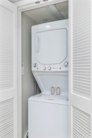 A compact laundry room with a front-loading washer and dryer, a control panel with various settings, and two detergent pods on the dryer. - Panaromic 2 /2 Condo, End Unit, Glass Wrapped, Highly Sought-after Floor Plan (Myrtle beach)