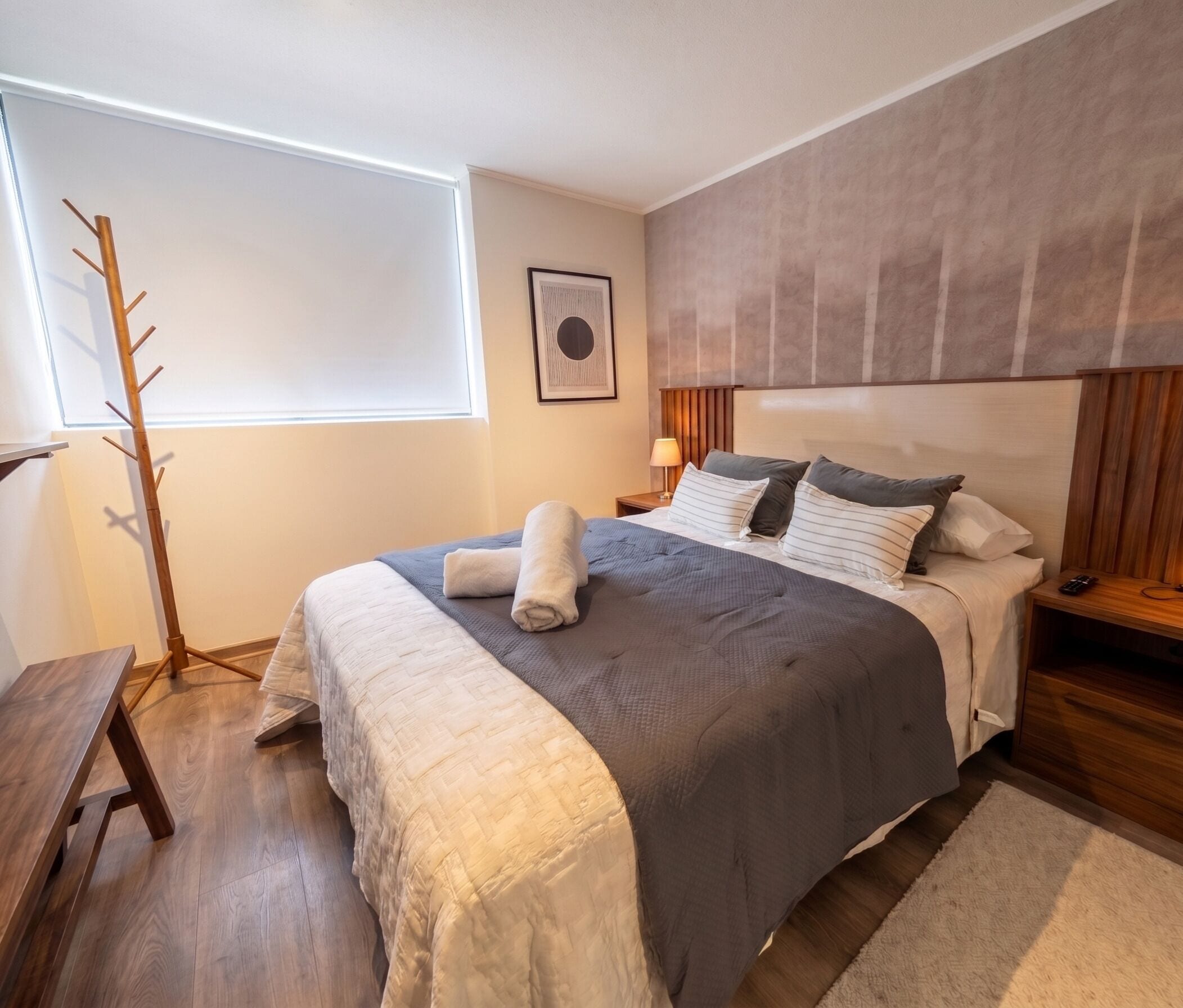 Un dormitorio con cama, mesitas de noche, lámpara, perchero y ventana.